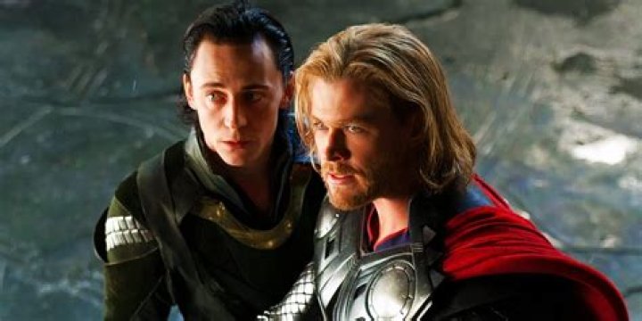 Loki and Thor are talking to each other in front of a dark and cloudy sky.